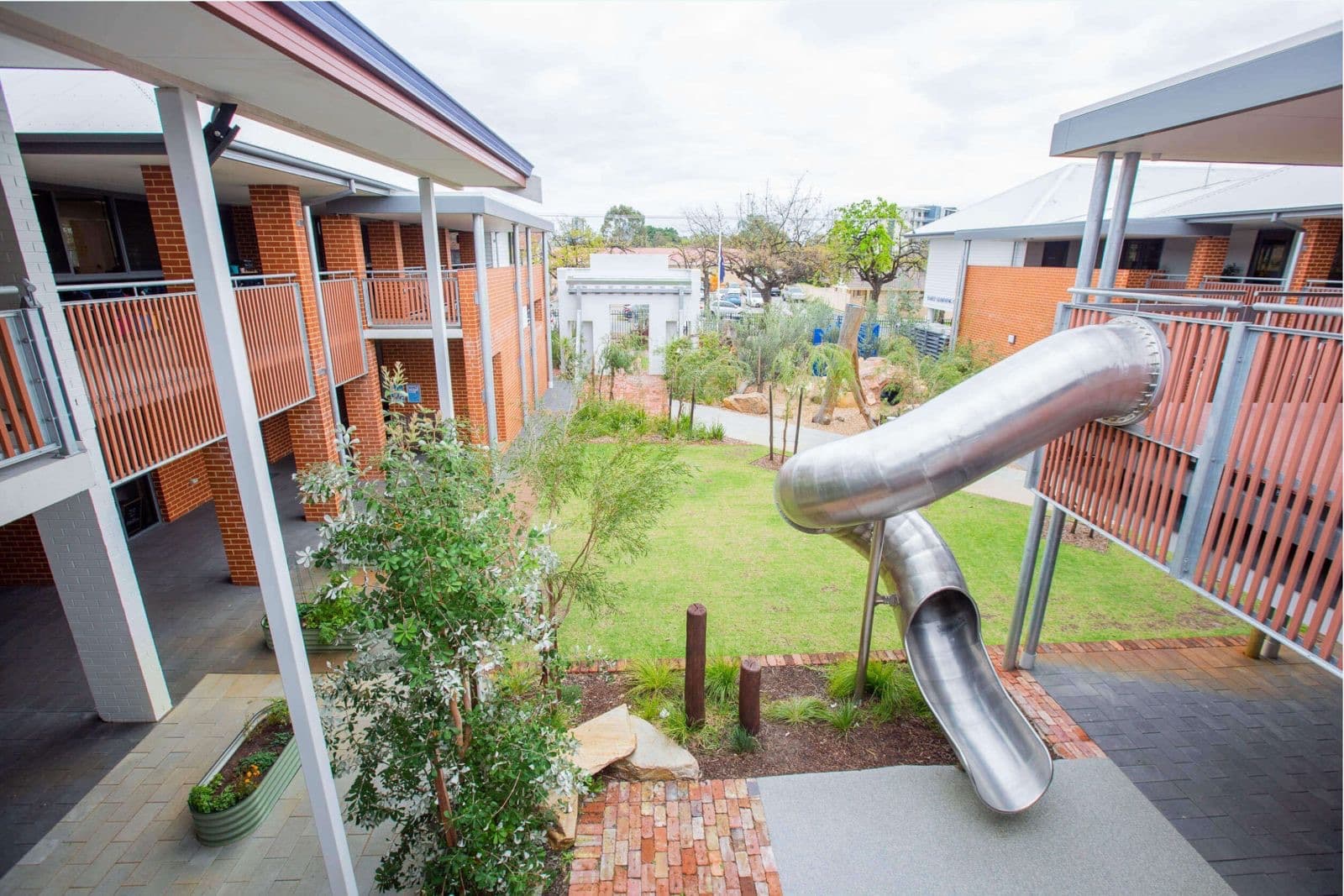A stainless steel tube slide integrated into a landscaped school courtyard