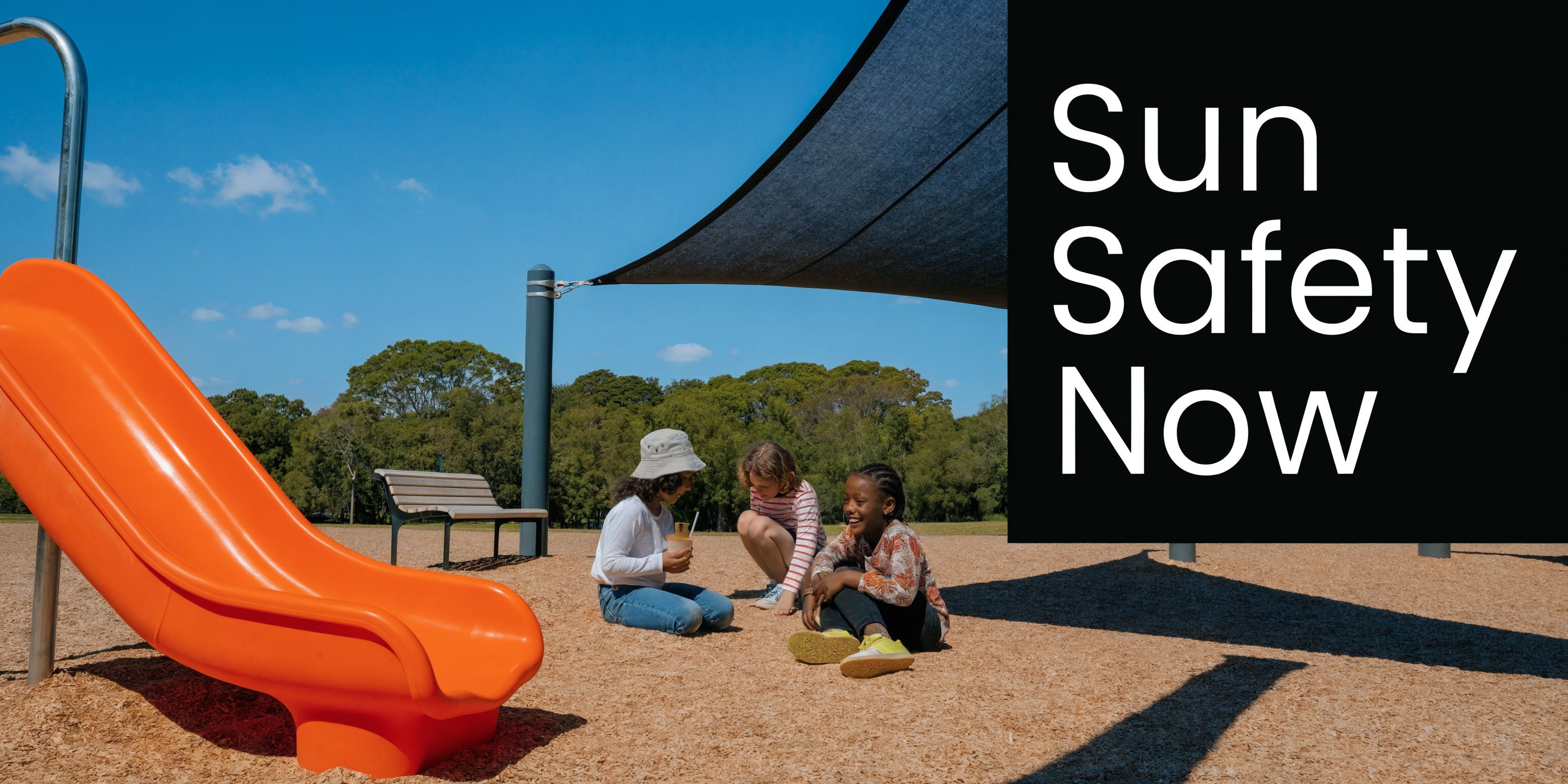 Three children playing together in the shade on a sunny day at a public playground.